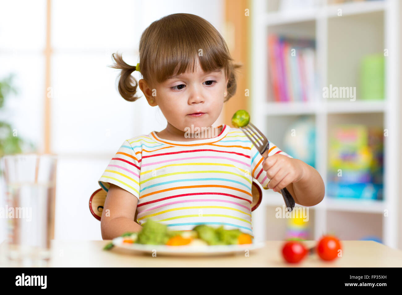 Kleines Mädchen untersucht Rosenkohl. Kind mit gesunden Lebensmitteln, die am Tisch im Kindergarten Stockfoto