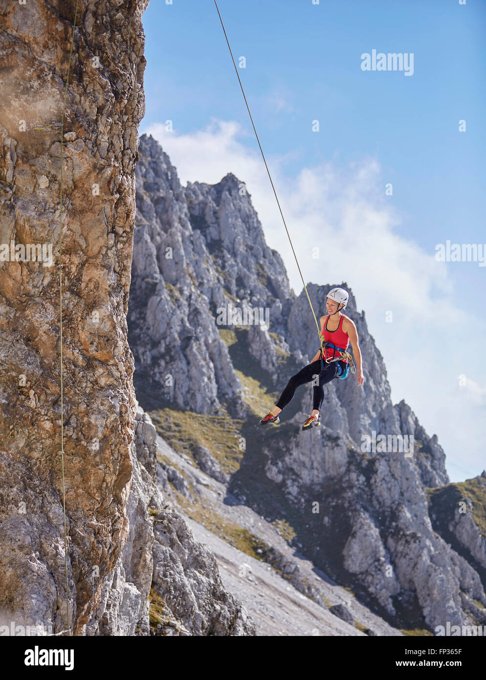 Kletterpflanze mit Helm schwingen am Kletterseil auf Felswand, Norden der Alpen, in der Nähe von Innsbruck, Tirol, Österreich Stockfoto