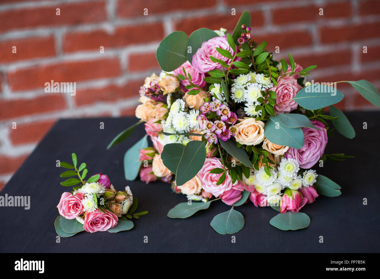 Wunderschönen Brautstrauß von frischen Blumen und Bräutigam Boutonniere auf alten schwarzen Holztisch in rotem Backstein-Mauer-Hintergrund Stockfoto
