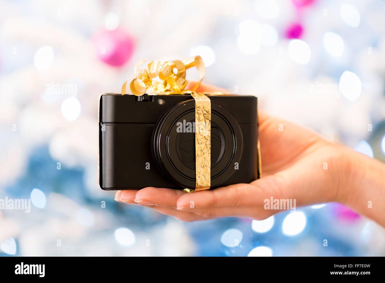 Frau präsentiert ein kompaktes Foto-Kamera-Geschenk in der Hand. Boke Weihnachtsbaum Hintergrund Stockfoto