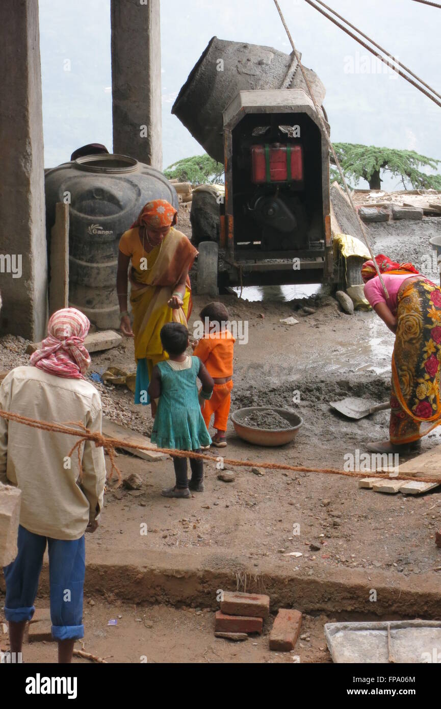 Eine Arbeitnehmerin auf einer indischen Baustelle nimmt eine vorübergehende Auszeit vom Mischen von Beton, um ihre kleinen Kinder neigen Stockfoto