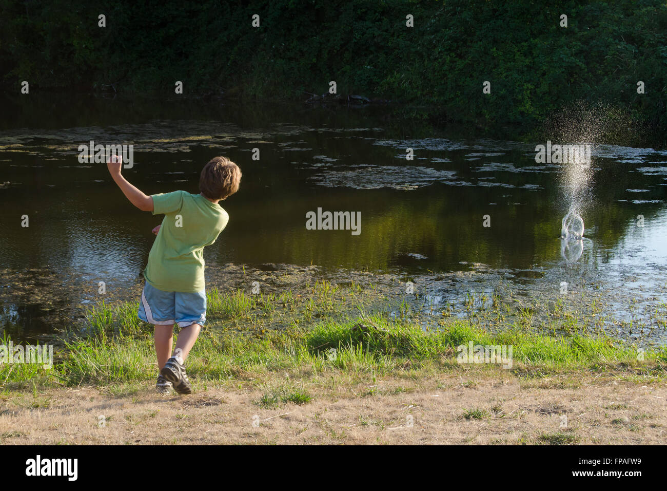 Ein kleiner Junge wirft Felsen in einen Teich in der späten Nachmittagssonne vielleicht greifen nach dem letzten Tage des Sommers vor Schulbeginn Stockfoto