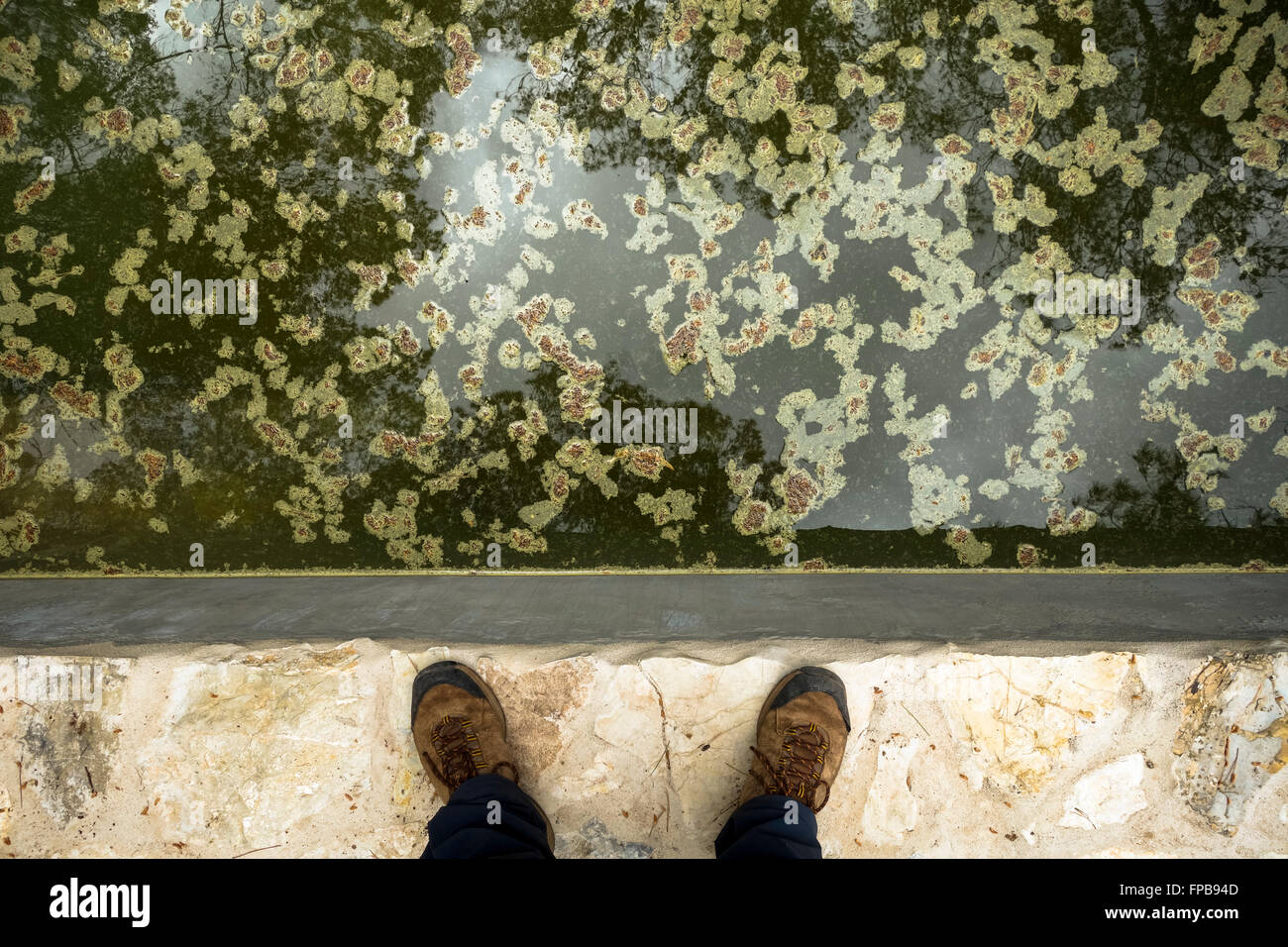 Zwei Beine mit Wandern Schuhwerk neben Schlamm, Grünalgen in künstlichen Teich. Stockfoto