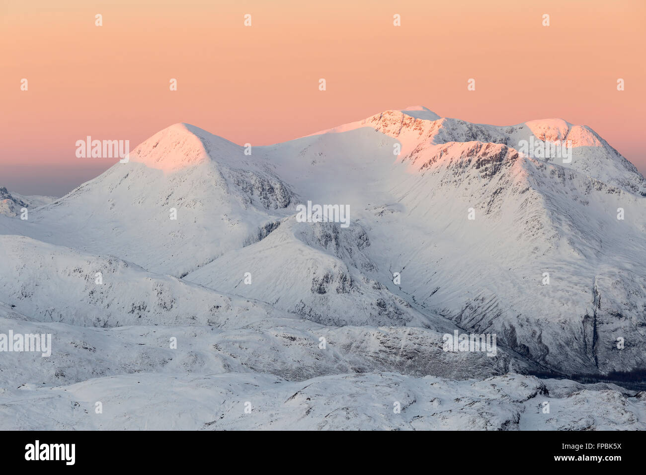 Die Gipfel auf Beinn Sgritheall werden rot, wenn sie von der aufgehenden Sonne, Glenelg, Schottland, von Sgurr Mhic Bharraich im Winter beleuchtet werden Stockfoto