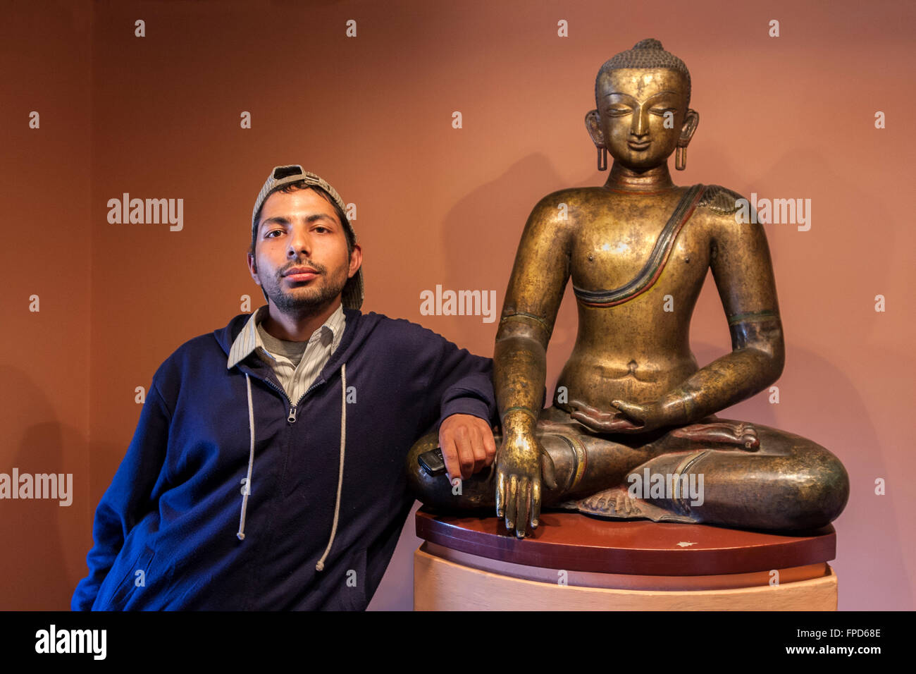 Nepal, Patan Museum.  Nepali hält sein Handy stehen neben einem Buddha in der Haltung des Sieges. Stockfoto