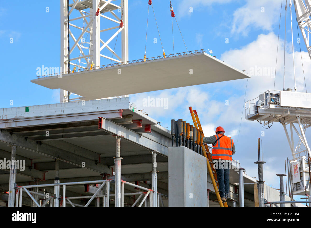 Website der Bauarbeiter auf Leiter als Kran Positionen großen Betonfertigteile Betonboden Panel auf neues Appartementhaus Gebäude in South London England UK Stockfoto