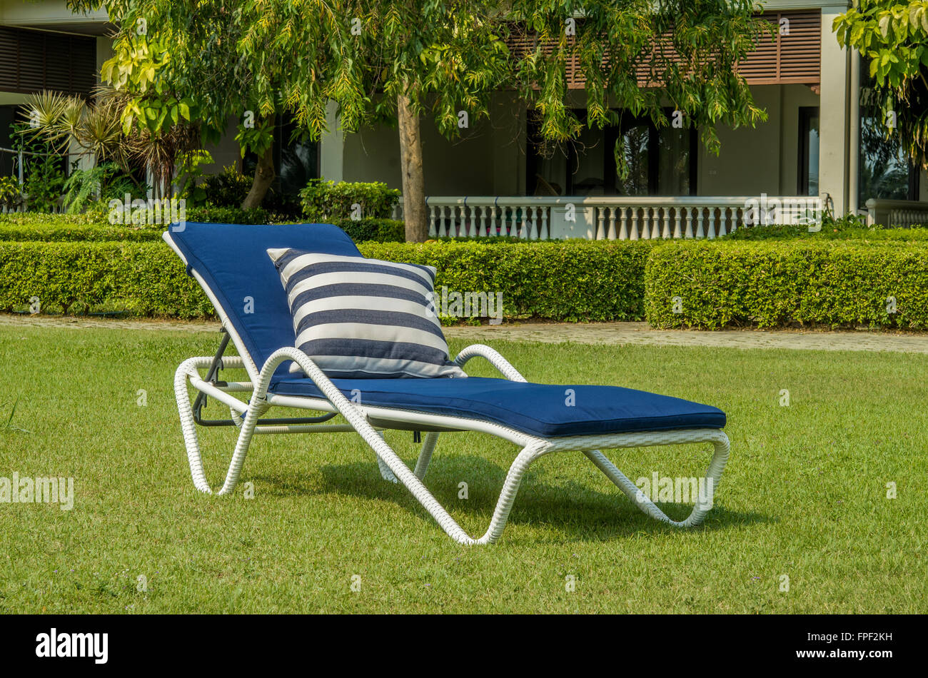 Rattan Sonnenliege mit blauen Kissen im grünen Garten Stockfoto