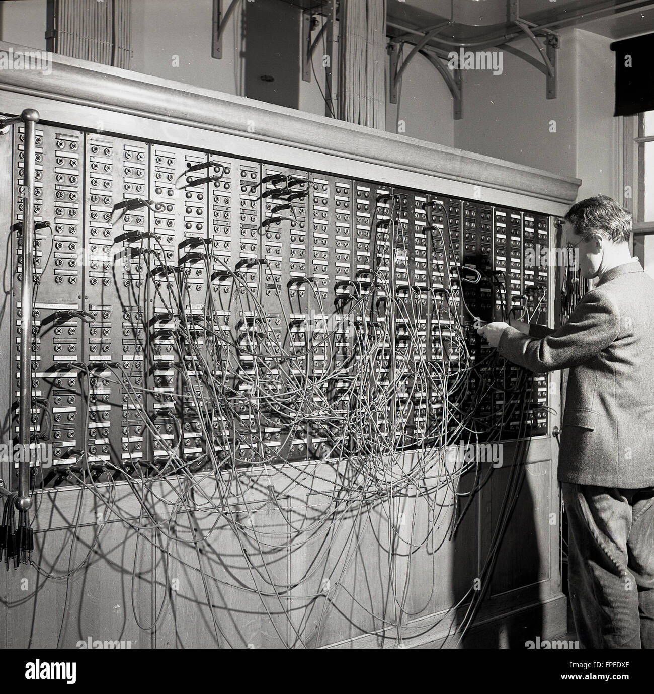 In den 1950er Jahren war ein männlicher Betreiber in einem Anzug, der Telefonkabel an einer Telefonzentrale an der transatlantischen Kabelstation in Waterville, Co. Kerry, Irland, wechselte. Das abgelegene Dorf Waterville war einst die Heimat einer der größten Kabelstationen der Welt und die erste erfolgreiche transatlantische Telegrafennachricht, die 1884 über das Kabel ging. In diesem Jahr hatte die Commerical Cable Co zwei Kabel über den Atlantik verlegt, die Kanada, Großbritannien und Frankreich über die Waterville-Station mit insgesamt 2,399 Meilen Kabel verbinden. Stockfoto