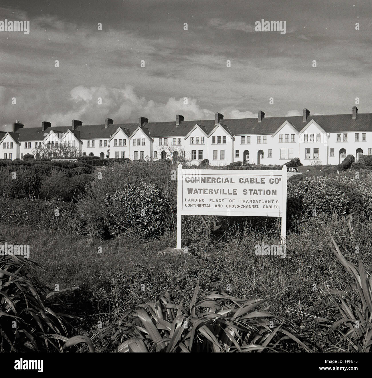 1950er Jahre, historisch, Schild mit dem Standort der Commercial Cable Co, Waterville Station, Irland. Das abgelegene Dorf Waterville, Co Kerry, war einst die Heimat einer der größten Kabelstationen der Welt und die erste erfolgreiche transatlantische Telegrafennachricht, die 1884 über das Kabel gesendet wurde. In diesem Jahr hatte die Commerical Cable Co zwei Kabel über den Atlantik verlegt, die Kanada, Großbritannien und Frankreich über die Waterville-Station mit insgesamt 2,399 Meilen Kabel verbinden. Es wurde ein großes Wohngebiet mit Blick auf den Atlantik gebaut, von dem Gebäude auf dem Bild zu sehen sind. Stockfoto