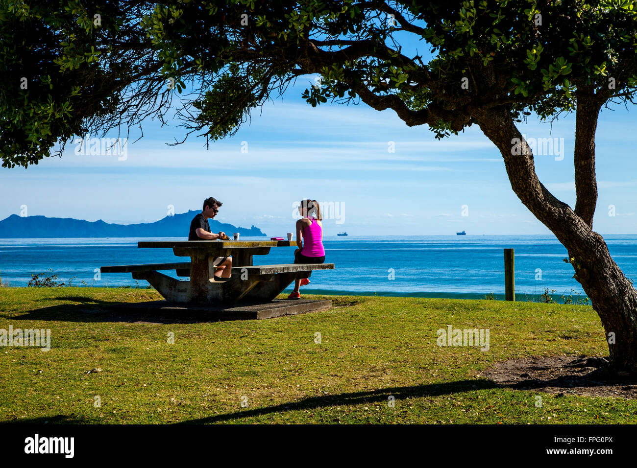 Ein paar Kaffeetrinken an einem Picknicktisch In Waipu Cove, Waipu, Northland, Neuseeland Stockfoto