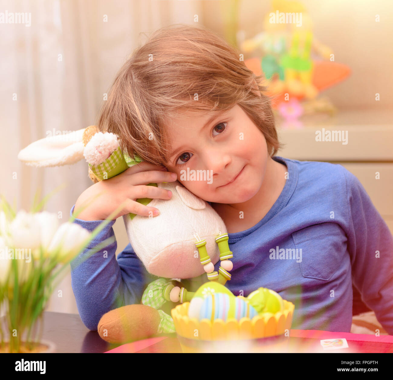 Porträt von niedlichen kleinen Jungen mit Ostern Hase Spielzeug sitzt auf der Küche in der Nähe von bunten Eiern, traditionelle festliche Speisen Stockfoto