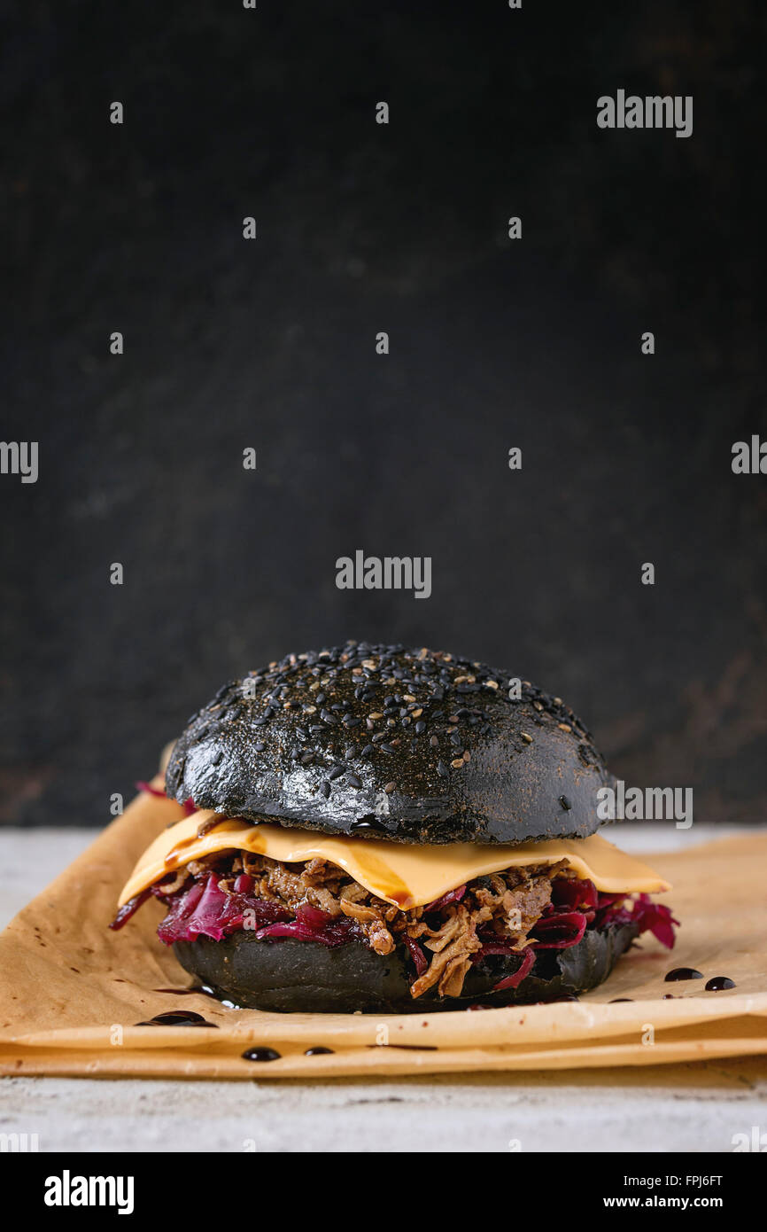 Schwarz-Burger mit Rindfleisch Eintöpfe, Käse, Rotkraut und Balsamico-Sauce, serviert auf Backpapier über grau verputzte Fläche mit bla Stockfoto