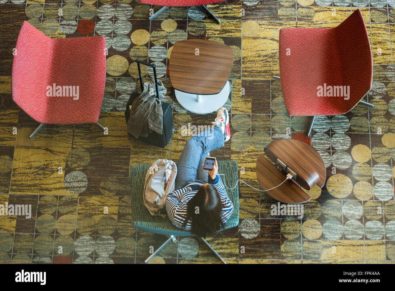 Blick von oben nach unten auf eine Reisende, die ihr Handy auflädt, während sie sich in der Abflughalle entspannt und auf ihren Flug wartet, Singapur Changi Airport. Stockfoto