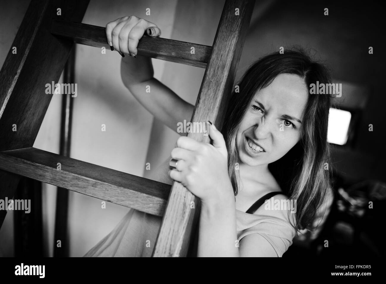 Verrückte Frau mit lustigem Gesicht stellt Erwachsene Mädchen mit verrückten Lächeln hängen alte Holzleiter Zimmer Interieur, horizontal Stockfoto