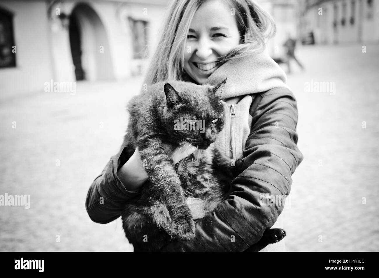 Frau umarmt böse Katze, junge Frau glücklich lächelnd und hält Tier in Armen und unglücklichen Katze will wieder nach unten gehen Stockfoto