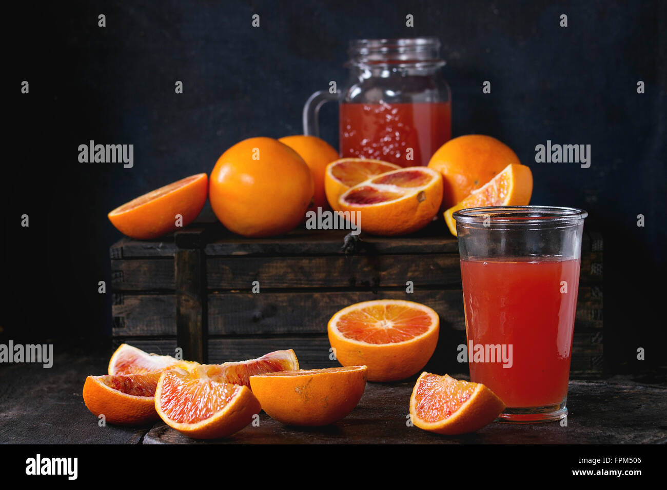 In Scheiben geschnitten und ganze sizilianischen Blutorangen und Glas frischen roten Orangensaft über alten Holztisch. Dunkel rustikalen Stil. Stockfoto