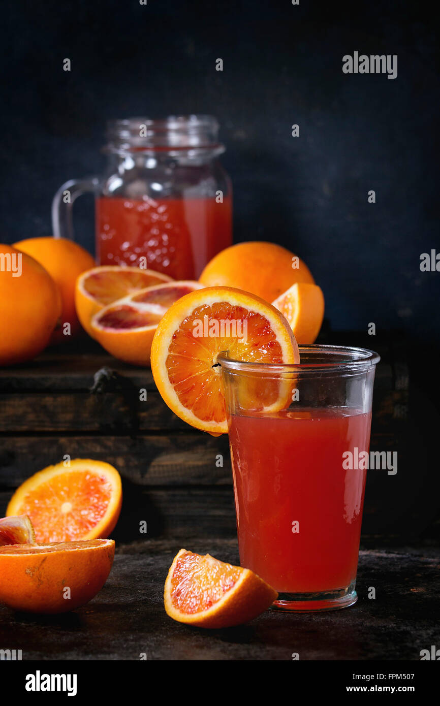 In Scheiben geschnitten und ganze sizilianischen Blutorangen und Glas frischen roten Orangensaft über alten Holztisch. Dunkel rustikalen Stil. Stockfoto