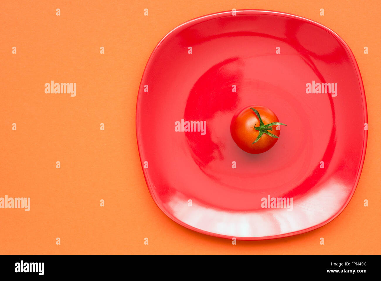 einzelne Tomatenfrucht auf die rote Platte und rotem Hintergrund Stockfoto