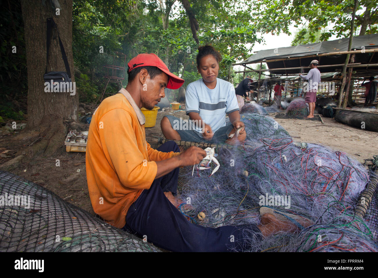 Asien, Thailand, Trang, Dorf Handwerker Fischer nehmen eine Krabbe aus einem großen Fischernetz, wenn sie es reparieren Stockfoto