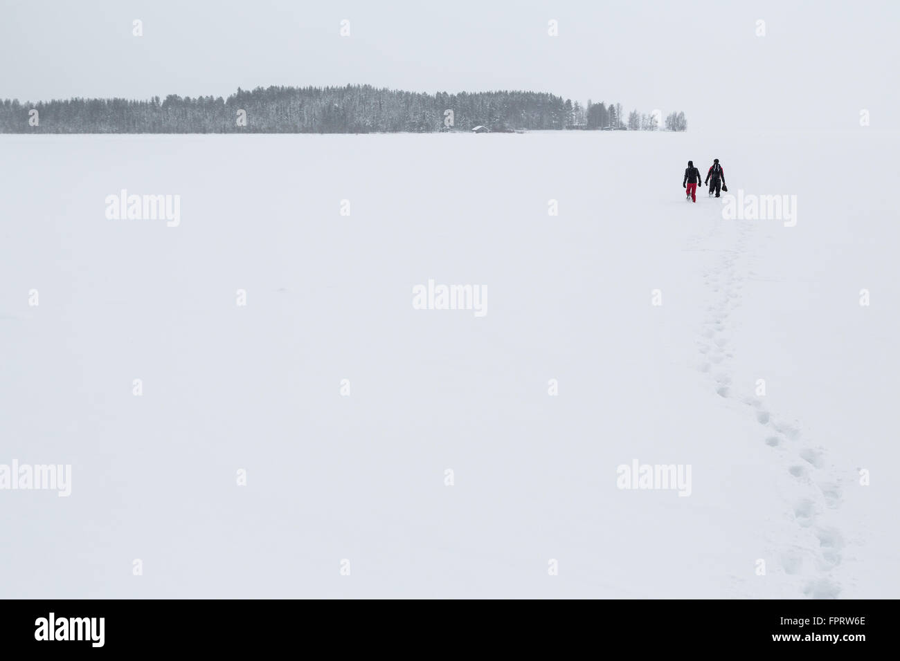 Zwei Menschen, die zu Fuß über einen gefrorenen See am Polarkreis vor Spuren Kivilompolio, in der Nähe von Rovaniemi, Lappland, Finnland Stockfoto