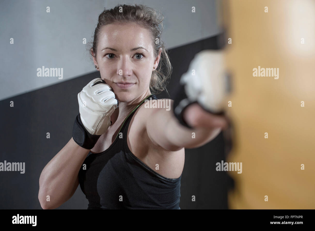 Junge Frau tun Krafttraining durch Stanzen am Boxsack in der Turnhalle, Bayern, Deutschland Stockfoto