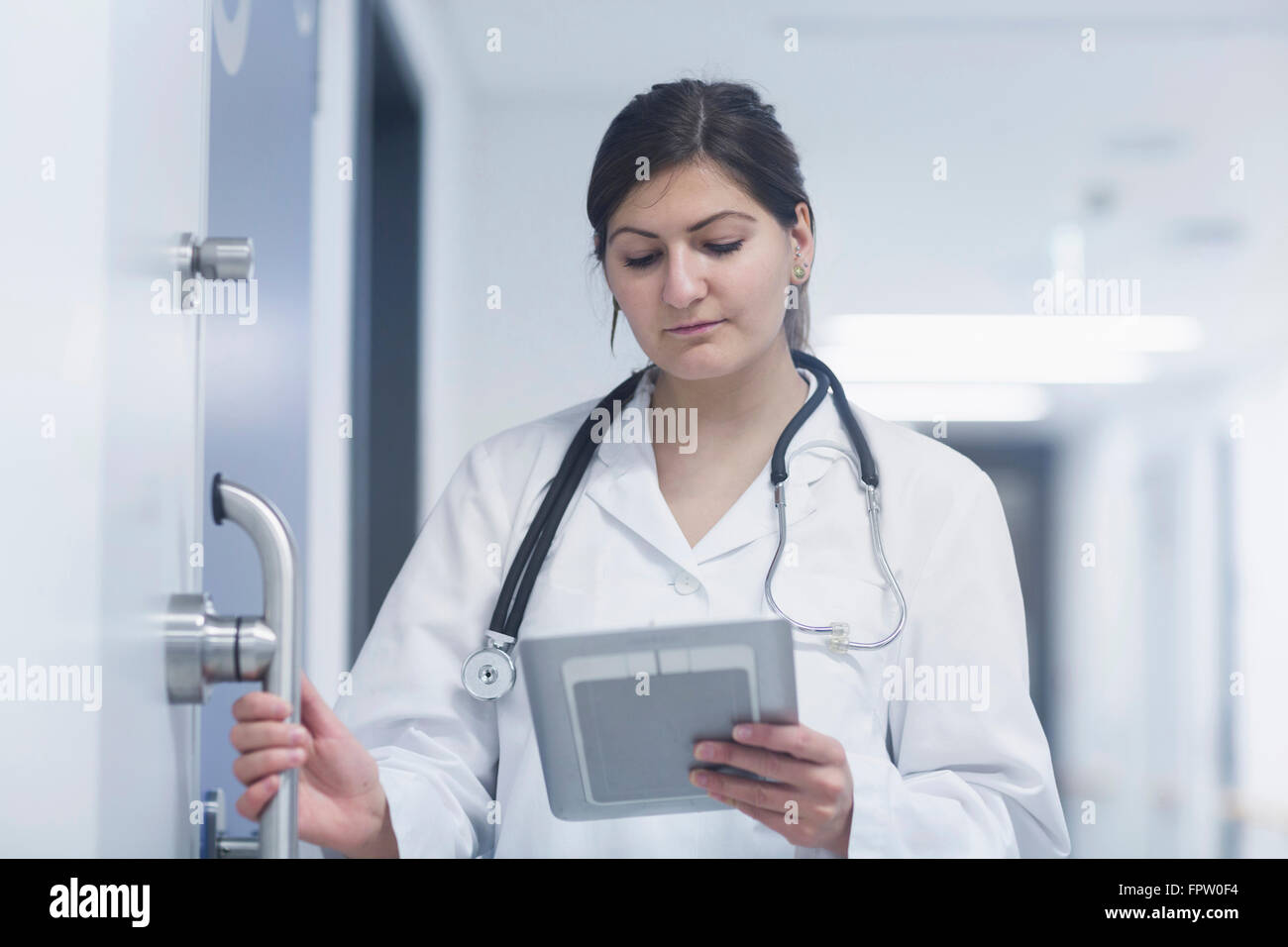 Junge Ärztin, die mit einem digitalen Tablet im Krankenhausflur, Freiburg Im Breisgau, Baden-Württemberg, Deutschland Stockfoto