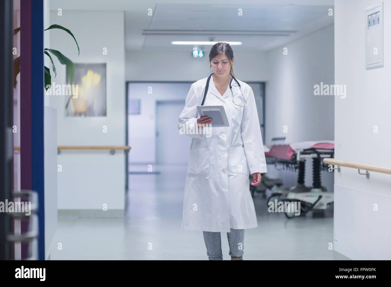 Junge Ärztin, die mit einem digitalen Tablet im Krankenhausflur, Freiburg Im Breisgau, Baden-Württemberg, Deutschland Stockfoto