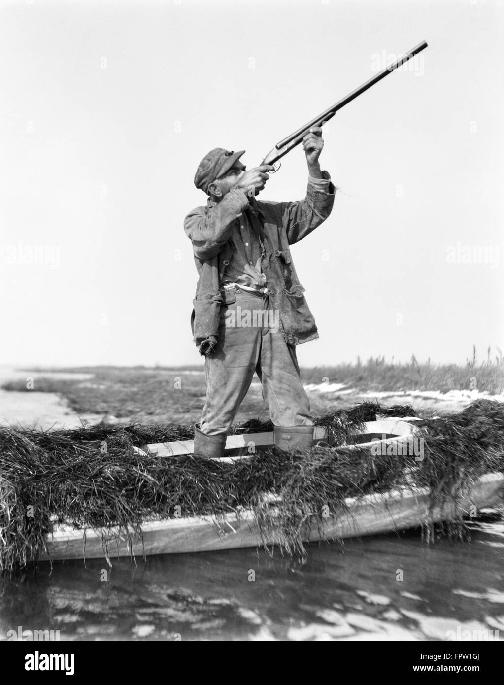 1920er Jahre Mann Entenjagd stehen IN SNEAKBOX Boot IN MARSH mit dem Ziel SCHROTFLINTE BARNEGAT BAY NEW JERSEY USA Stockfoto