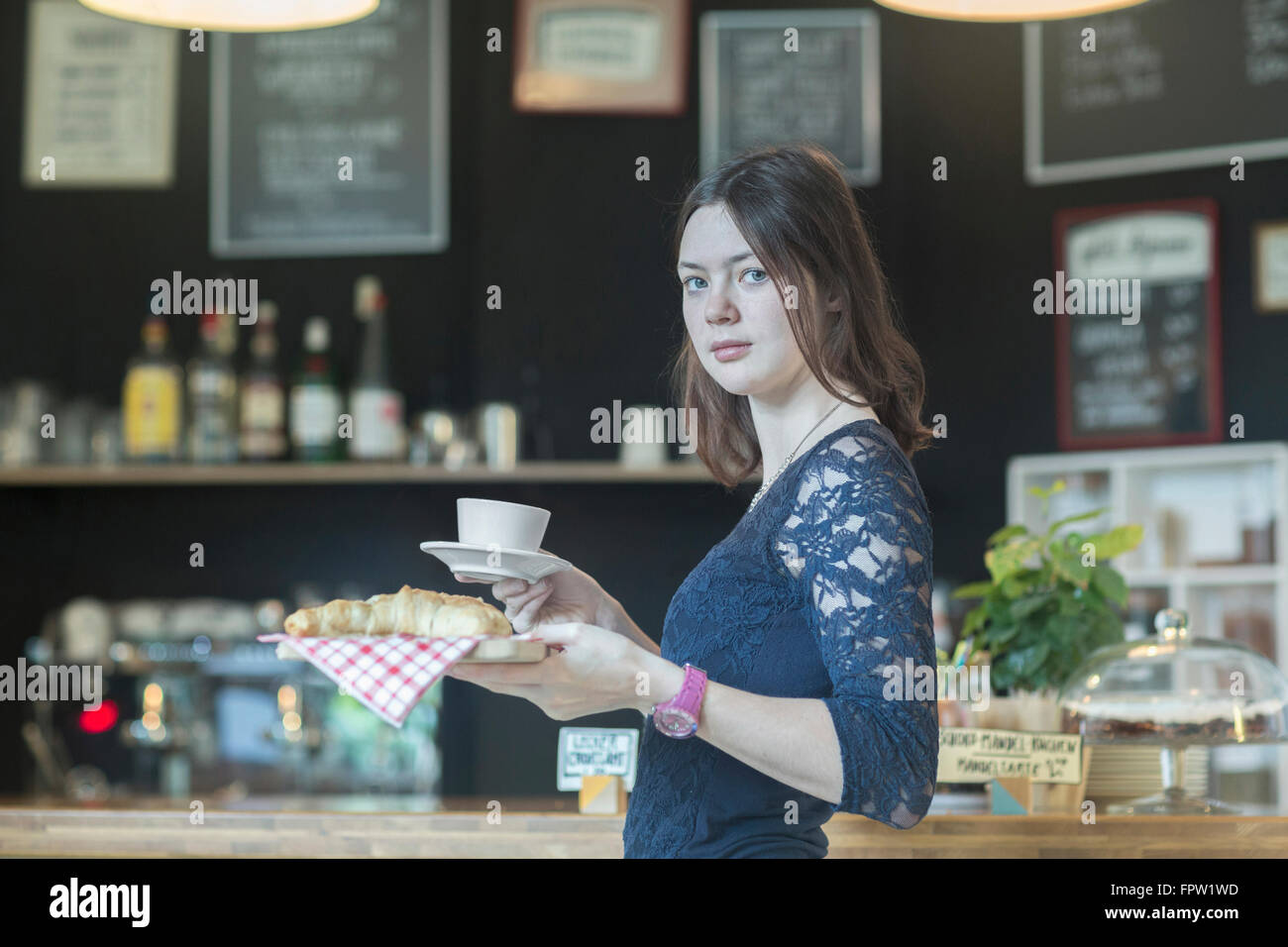 Junge Kellnerin serviert Kaffee und Croissant in Coffee-Shop, Freiburg Im Breisgau, Baden-Württemberg, Deutschland Stockfoto