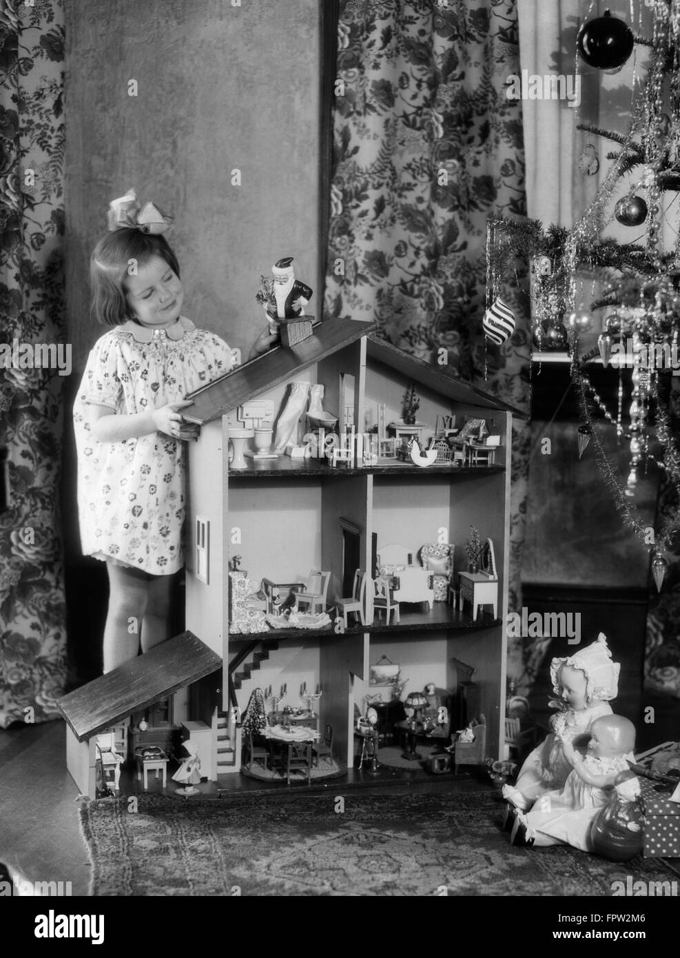 1920S 1930S LÄCHELNDES MÄDCHEN MIT GROßEN PUPPENHAUS UND WEIHNACHTSBAUM Stockfoto