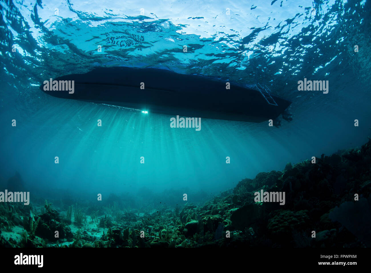 Sonnenlicht Silhouetten ein Boot schwebt über einem Korallenriff in der Karibik. Stockfoto
