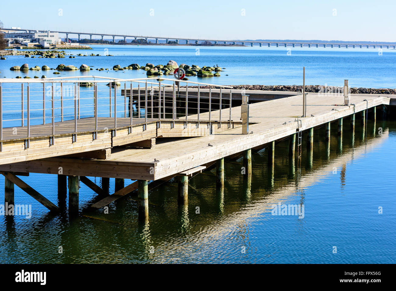 Ein hölzerner Pier erstreckt sich in das Meer mit der Öland-Brücke im Hintergrund. Stockfoto