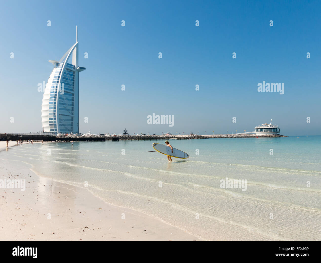 Frau mit Surfbrett am Strand von Jumeirah Burj al Arab Hotel im Hintergrund, Dubai, Vereinigte Arabische Emirate Stockfoto