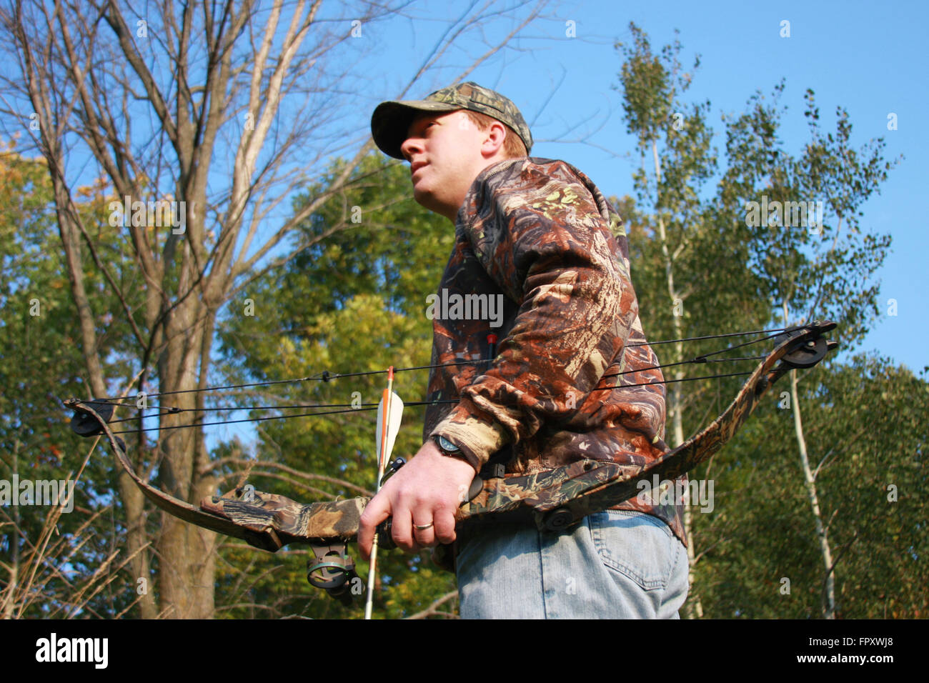 Bow Hunter in Tarnung vor dem bewaldeten Hintergrund Stockfoto