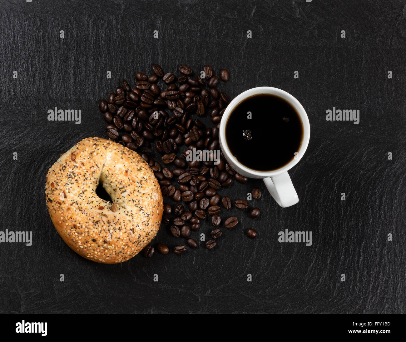 Draufsicht auf frischem dunklen Kaffee, große ausgesät Bagel und gerösteten Bohnen auf Schiefer Naturstein. Stockfoto