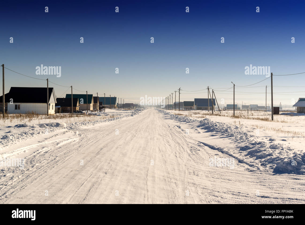 Winter schneebedeckte Straße führt durch eine inländische Dorf bis zum Horizont. Kristallklarer blauer Himmel hängt über Kopf. Die abgenutzten r Stockfoto