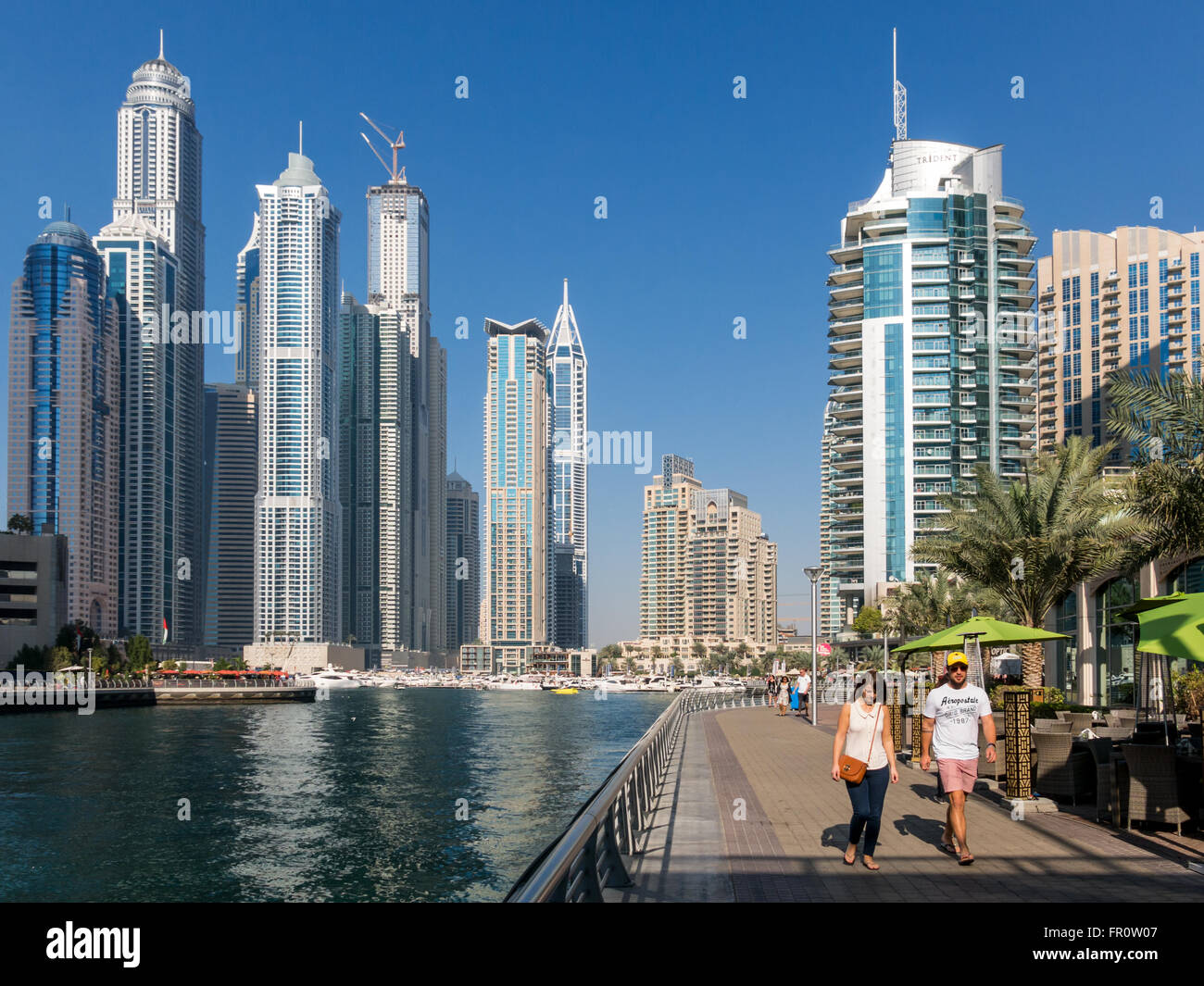 Menschen zu Fuß auf der Promenade, Boote und Highrise Waterfront-Gebäude im Stadtteil Marina von Dubai, Vereinigte Arabische Emirate Stockfoto
