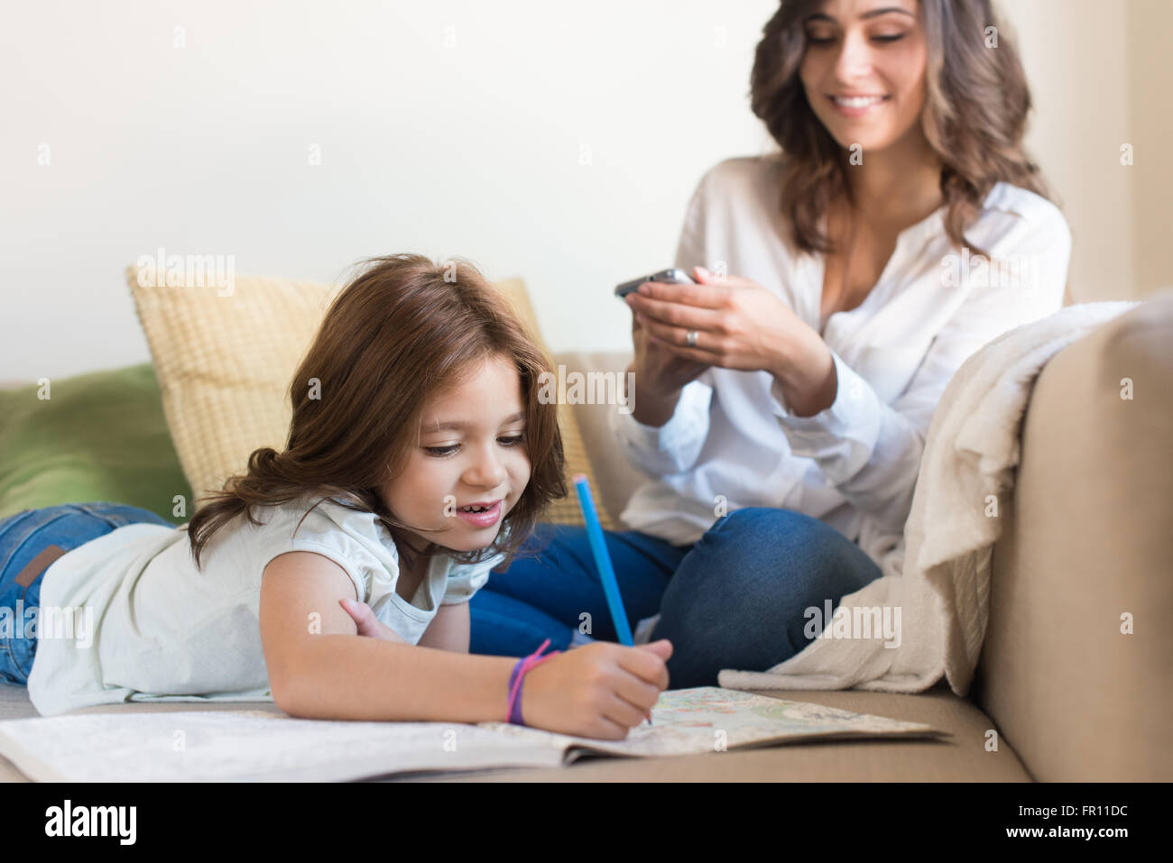 Kleines Mädchen malen im Wohnzimmer, während Mama mit Internet verbunden ist Stockfoto