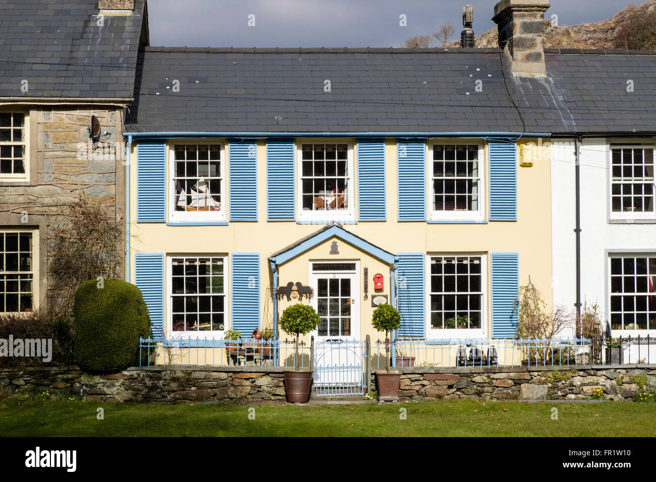 Hübsches traditionelles walisisches Cottage mit blauen Fensterläden auf Dorfgrün in Snowdonia. Beddgelert, Gwynedd, Nordwales, Großbritannien Stockfoto
