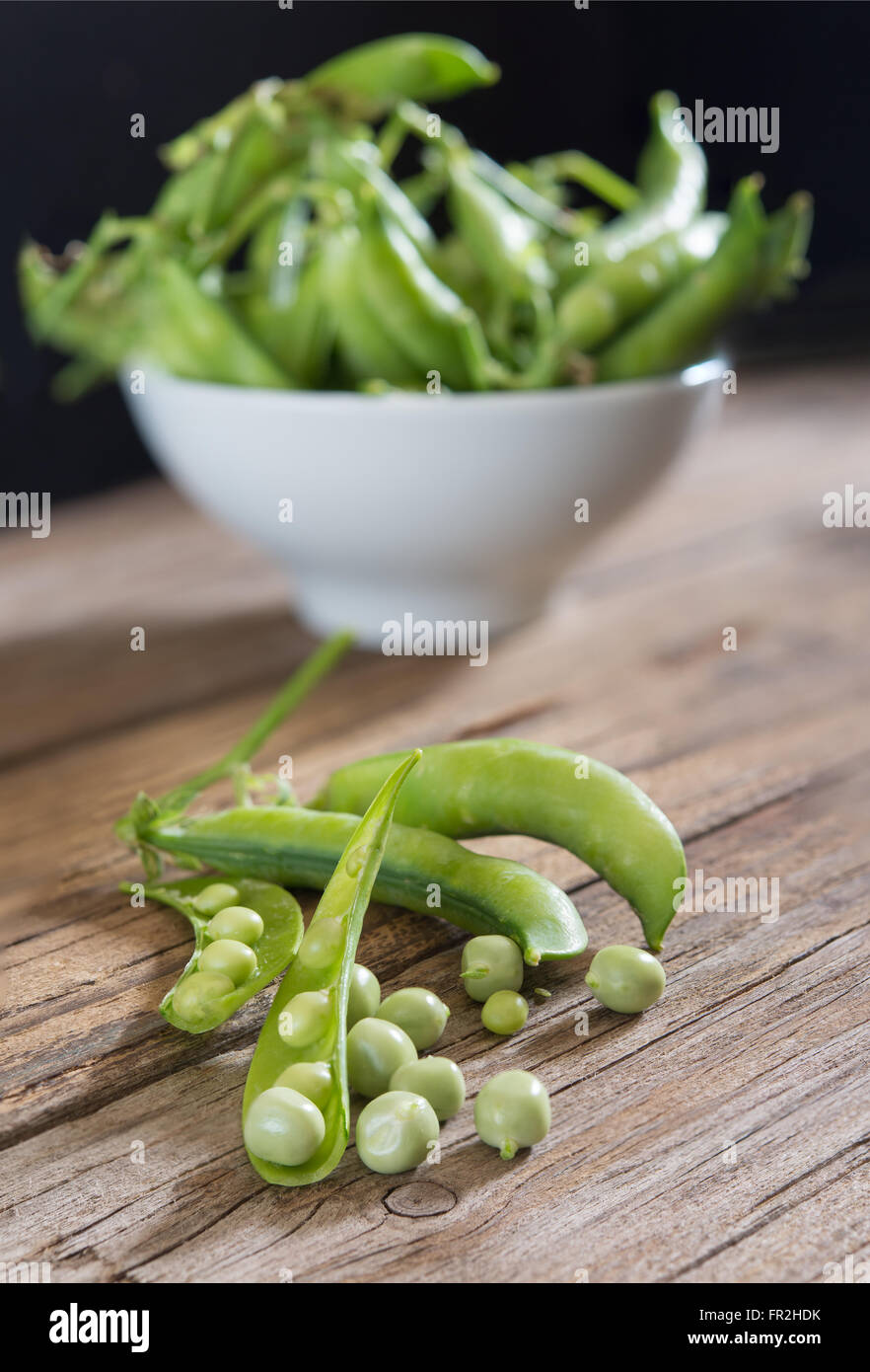 Frische grüne Erbsen auf Holztisch mit schwarzem Hintergrund Stockfoto