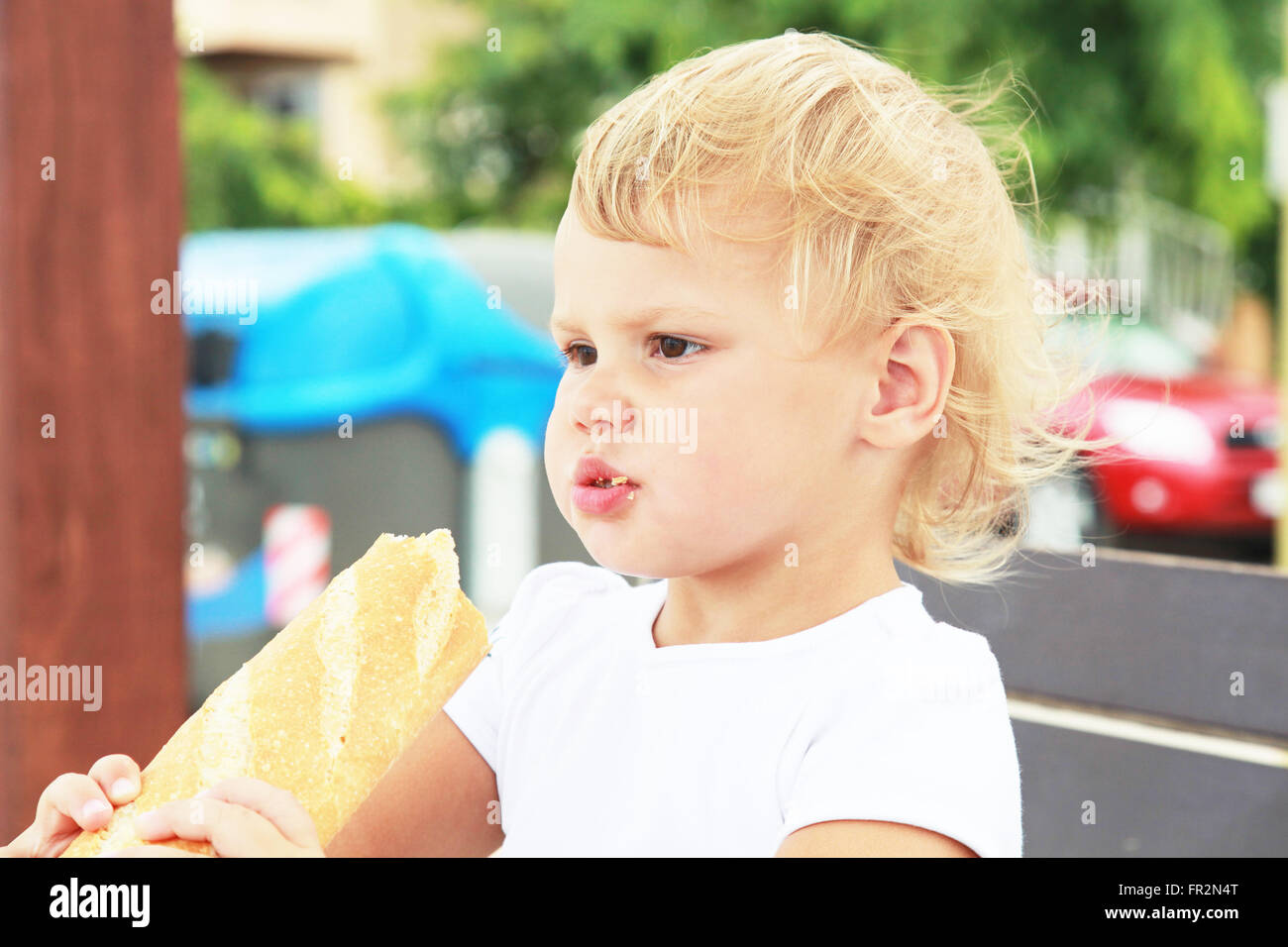 Outdoor Closeup Portrait von niedlichen kaukasischen blonde Babymädchen essen große französische baguette Stockfoto