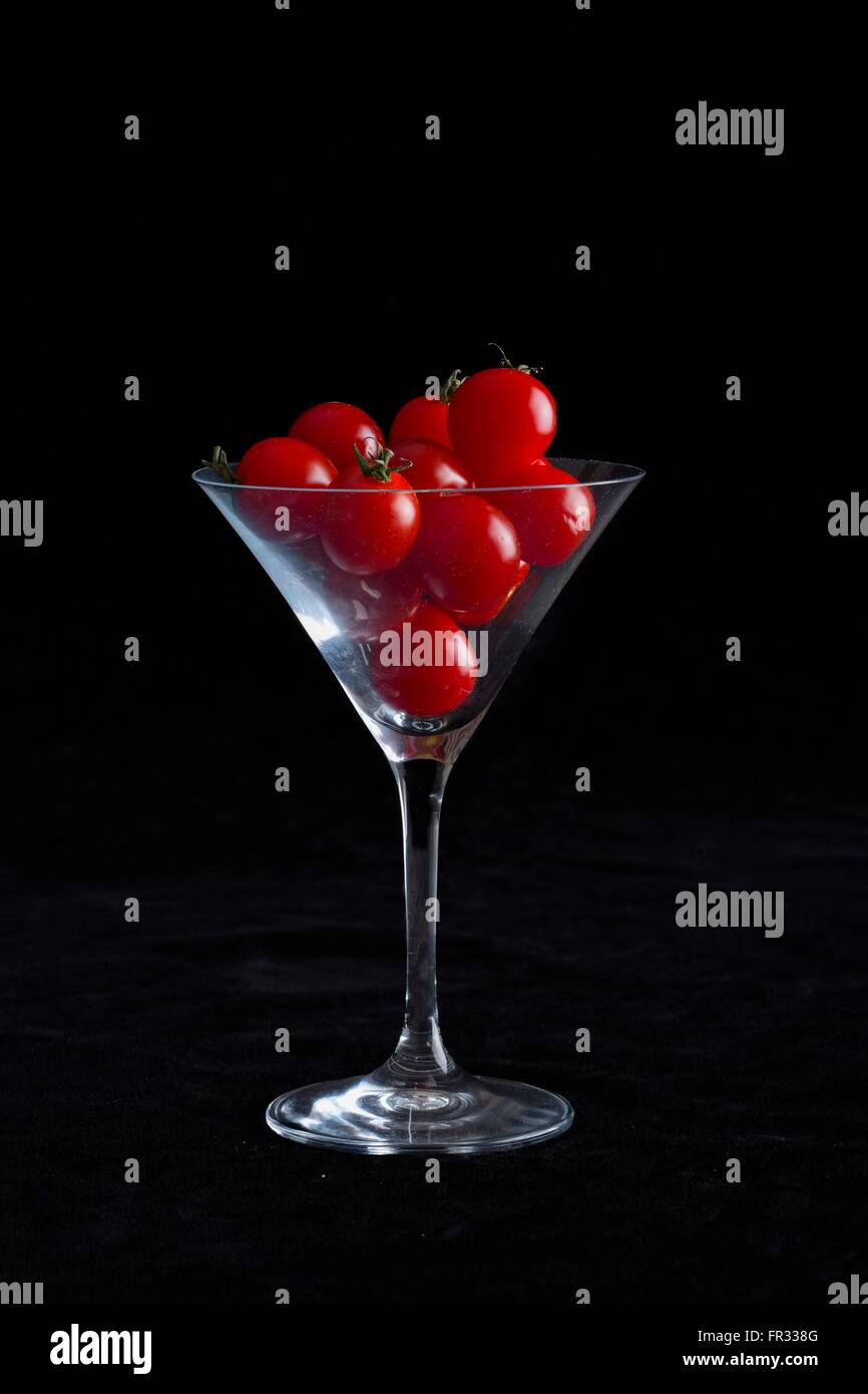 Ein low-Key, dramatische Bild von einem Martini-Glas gefüllt mit Cherry-Tomaten auf einem schwarzen Hintergrund Stockfoto