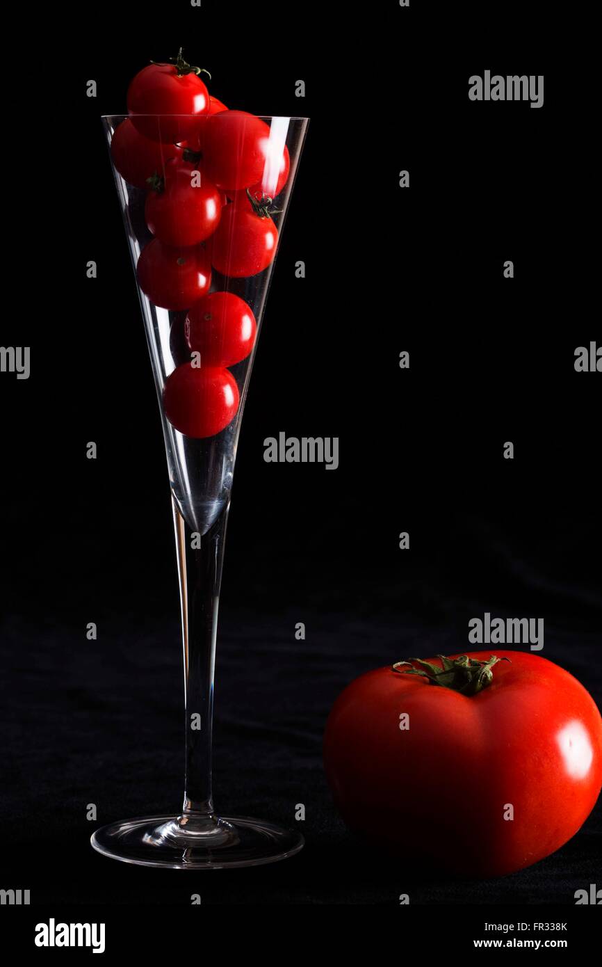 Niedrige Schlüsselbild ein Sektglas gefüllt mit Cherry-Tomaten mit großen Rindfleisch Tomaten auf der Seite und einem schwarzen Hintergrund Stockfoto