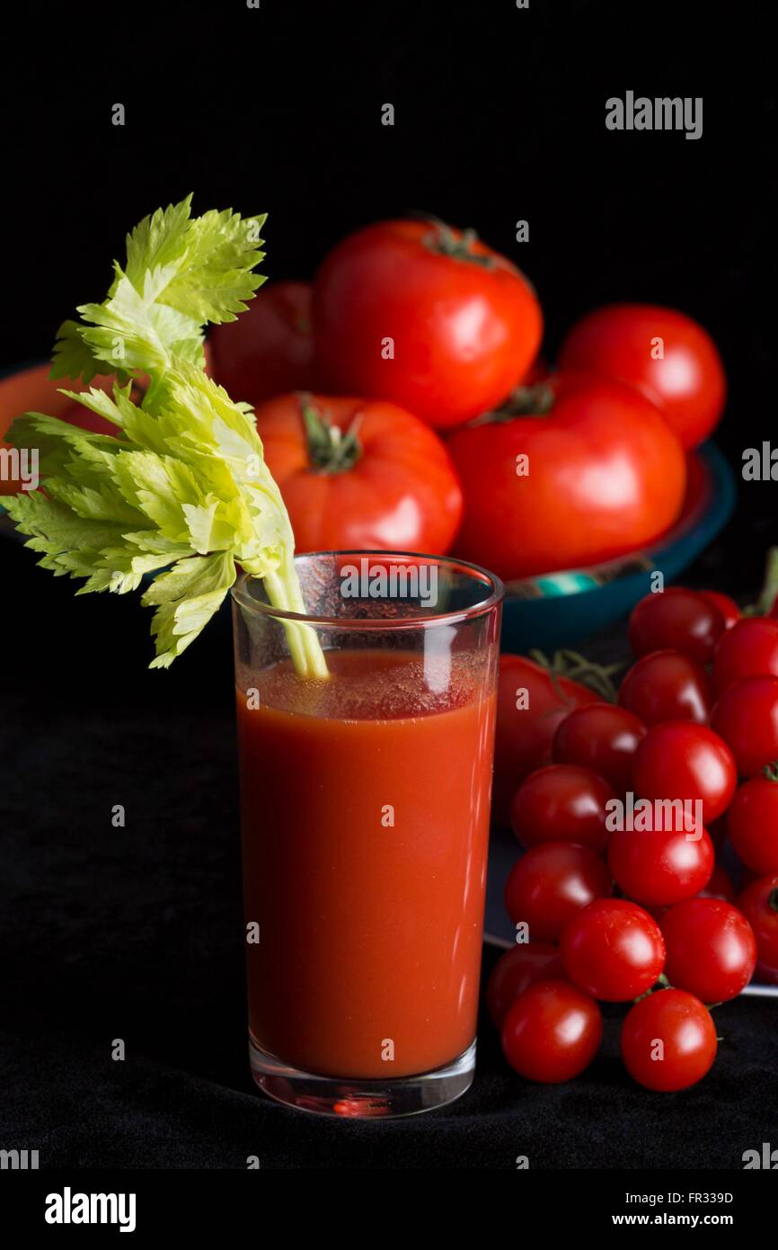 Bloody Mary cocktail mit einem Stiel von Sellerie und umgeben von frischen Tomaten in verschiedenen Größen auf einem schwarzen Hintergrund Stockfoto