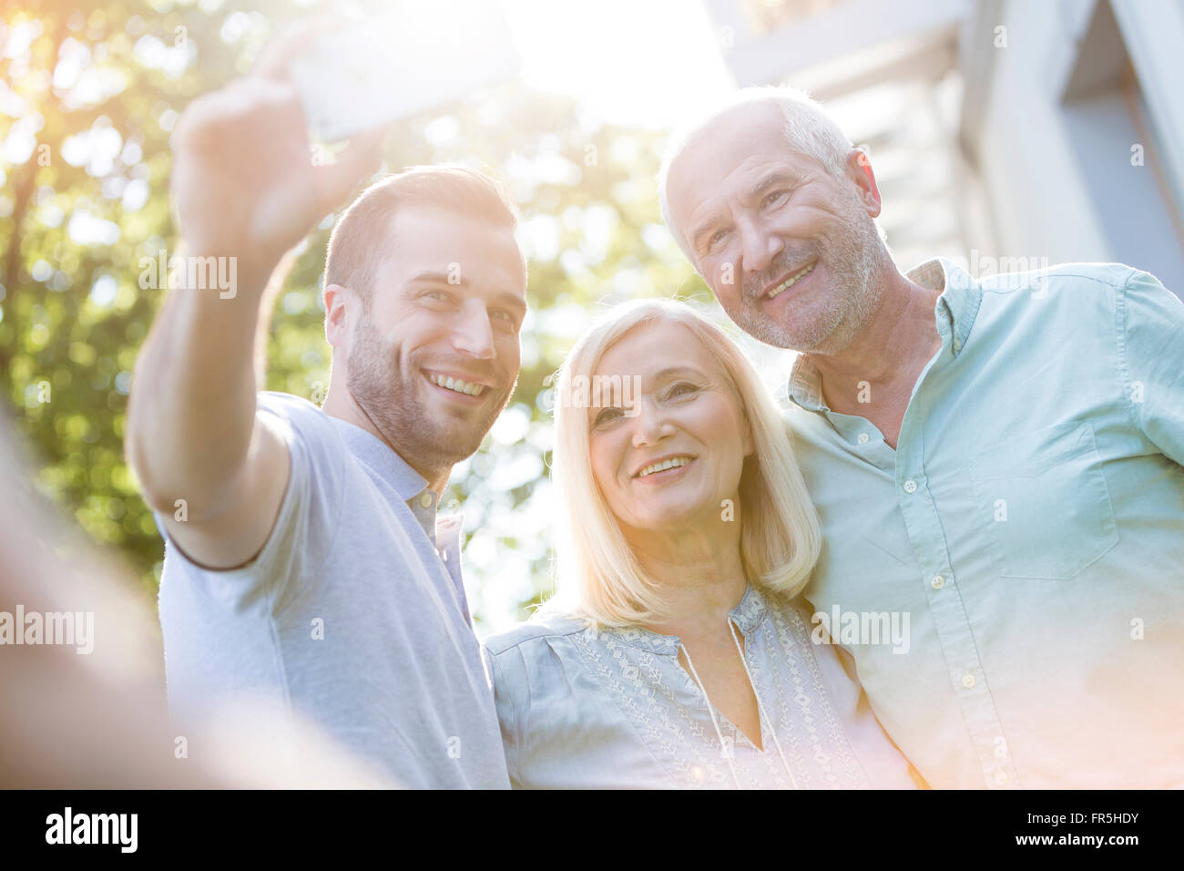 Lächelnd, älteres Paar und erwachsener Sohn nehmen Selfie im freien Stockfoto
