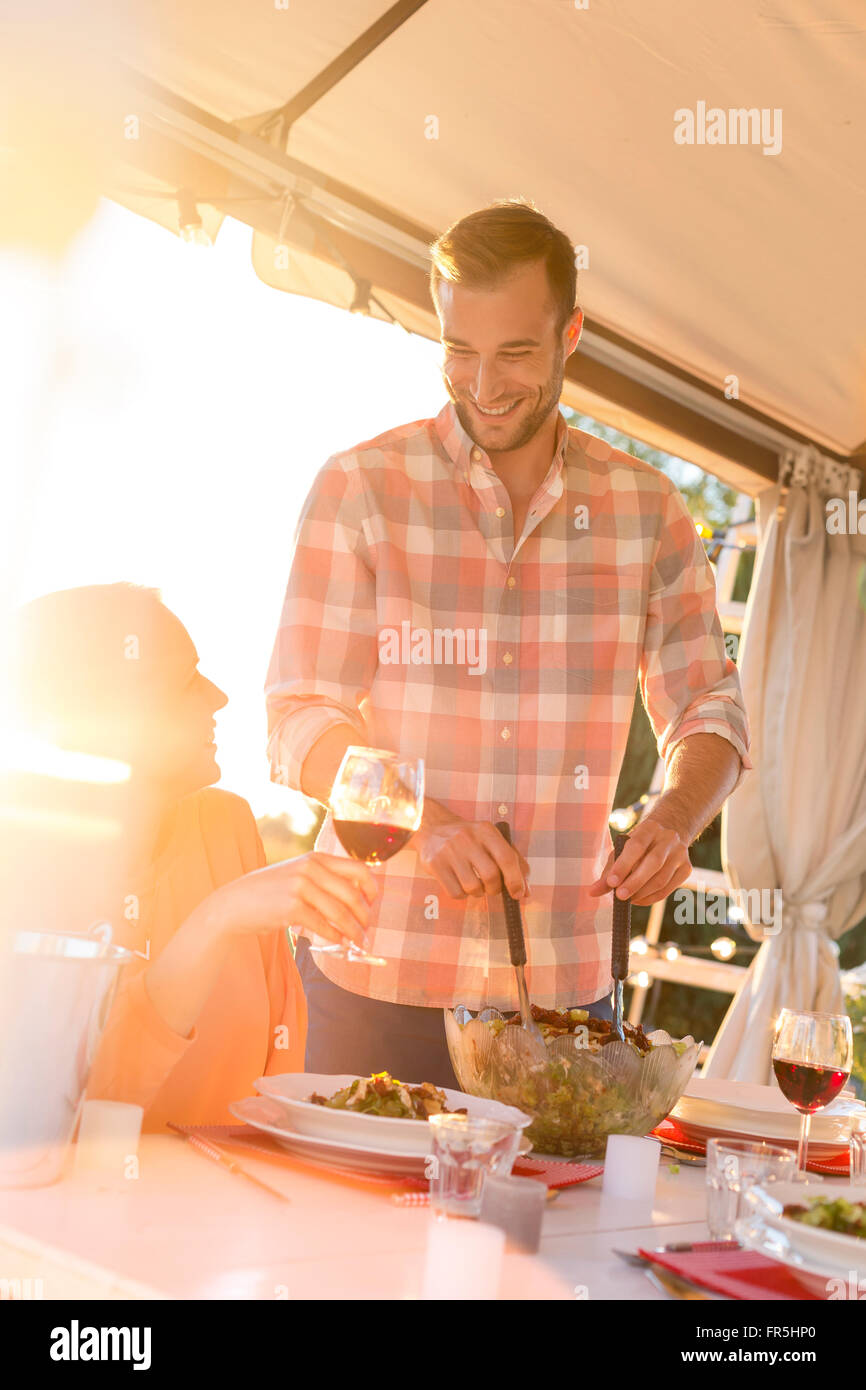 Junger Mann Portion Salat Frau Weintrinken an sonnigen Patio Tisch Stockfoto