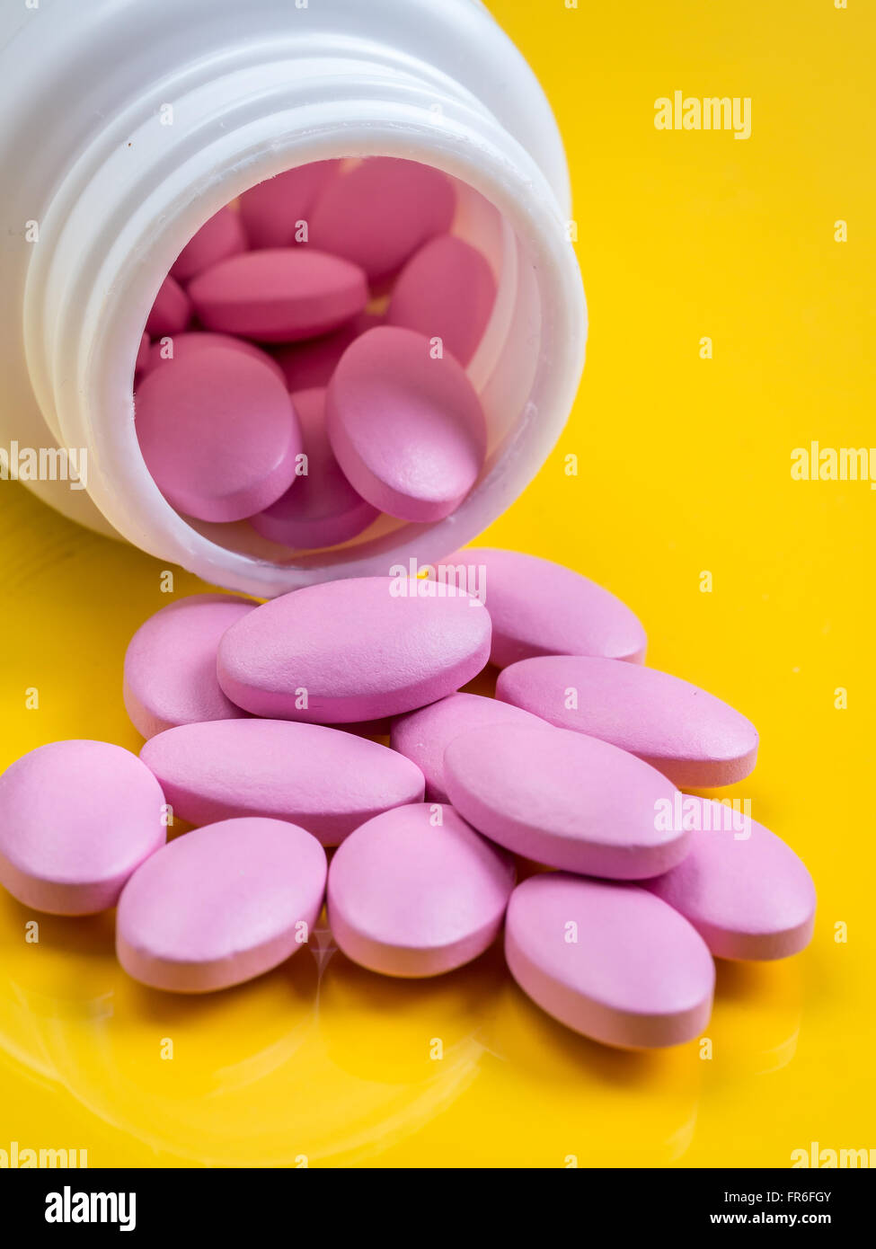 Rosa Tabletten übergreifen gelben Hintergrund aus weißem Kunststoff-Flasche Stockfoto