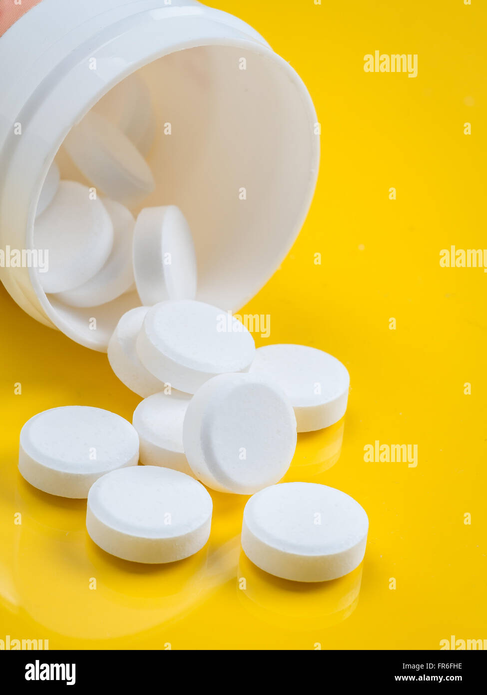 Weiße Tabletten übergreifen gelben Hintergrund aus weißem Kunststoff-Flasche Stockfoto