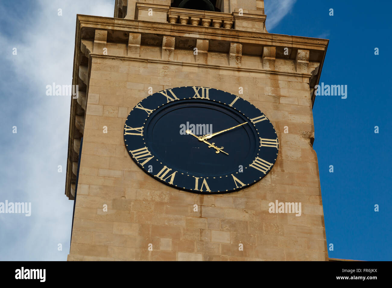 Blick auf eine Kirche in Valletta Malta mit Kalkstein Glockenturm Uhrturm, auf blauen Wolkenhimmel Hintergrund. Stockfoto