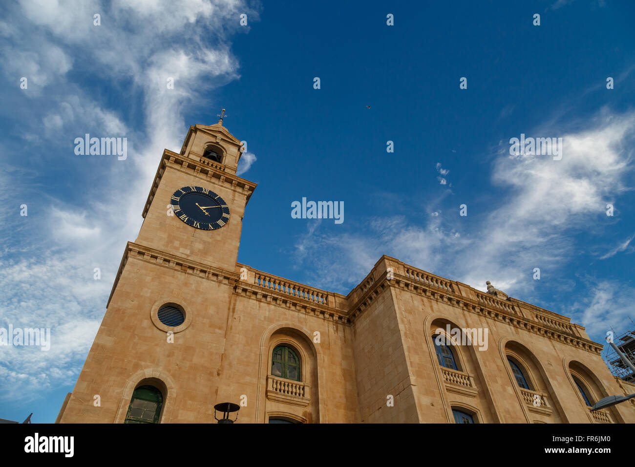 Blick auf eine Kirche in Valletta Malta mit Kalkstein Glockenturm Uhrturm, auf blauen Wolkenhimmel Hintergrund. Stockfoto
